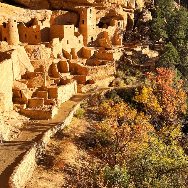 Afternoon sun glows on  an ancient sandstone village built in an alcove with leaves in autumn color