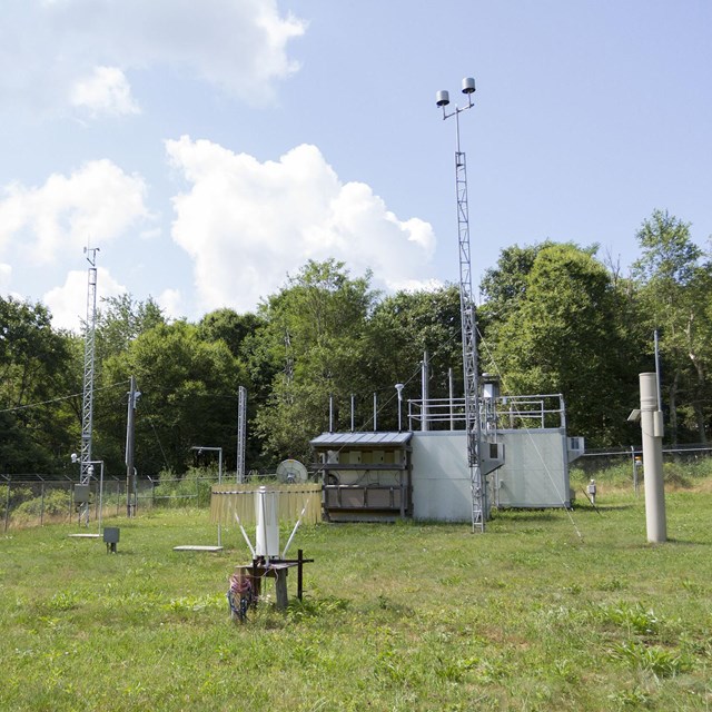 Climate monitoring station in a grassy clearing, with many scientific instruments scattered about.