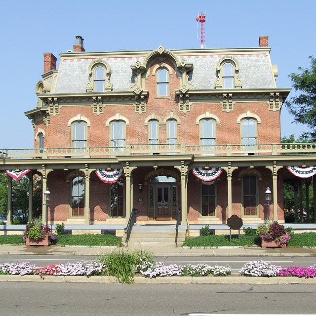 Front view of a large three story red brick house with a large covered porch. 