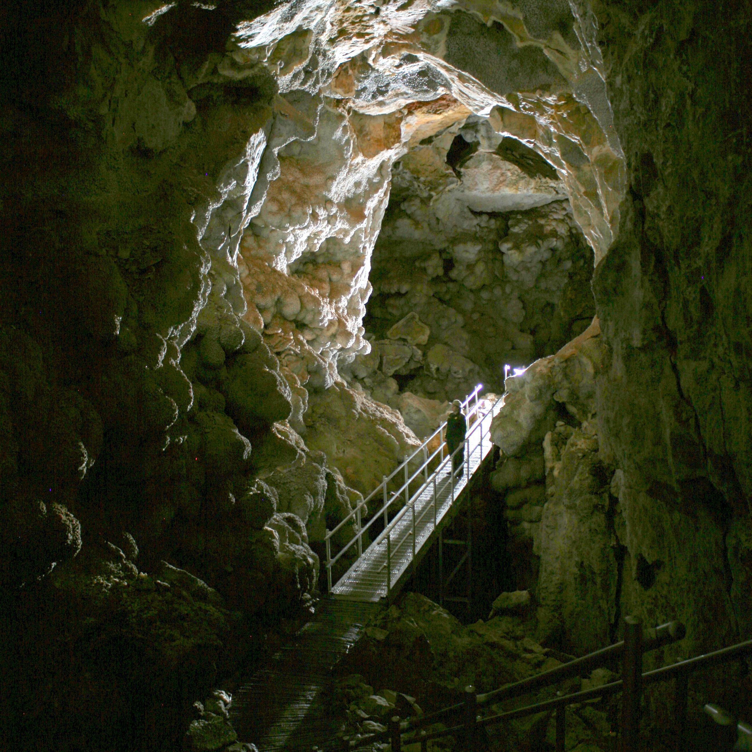 A park ranger stands on a metal platform within a long cave passageway with a vaulted ceiling.