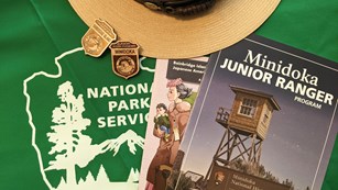 Junior ranger booklets and badges on a table with a ranger hat and a green NPS tablecloth.