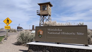 The Minidoka entrance sign along Hunt Road, with the guard tower rising up behind it.