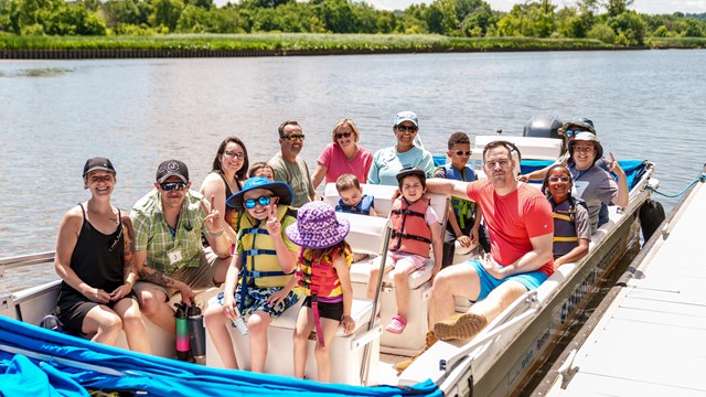 About a dozen adults and kids pose for a photo on a boat next to a dock.