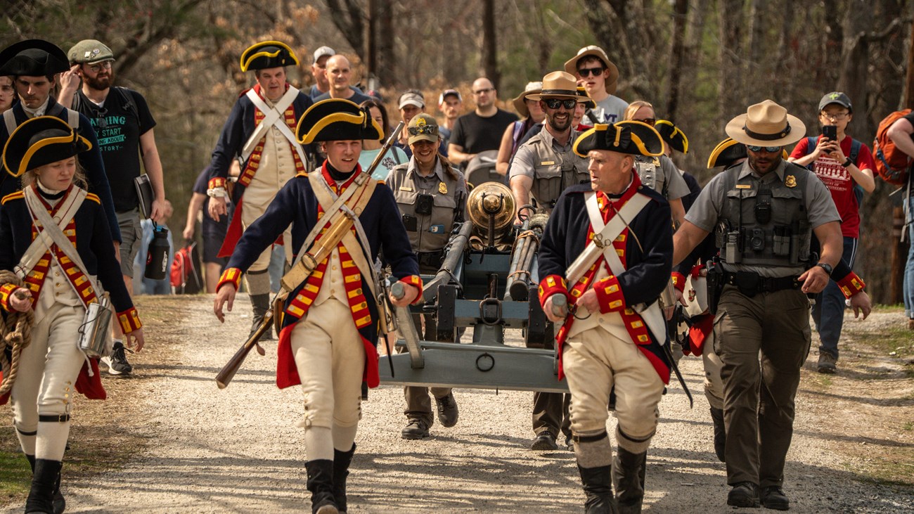 A group of royal artillery reenactors and park rangers pull a cannon down a road.