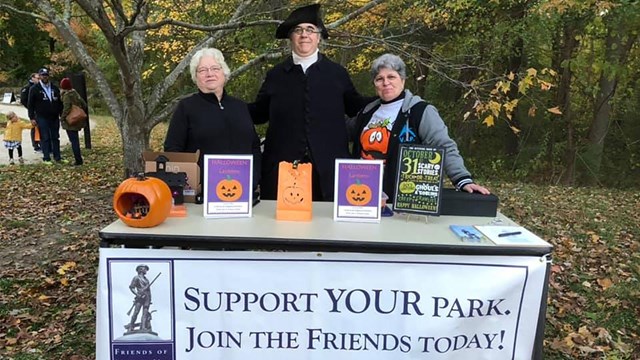 Three people pose behind a large table with banner reading Support Your Park Join The friends Today