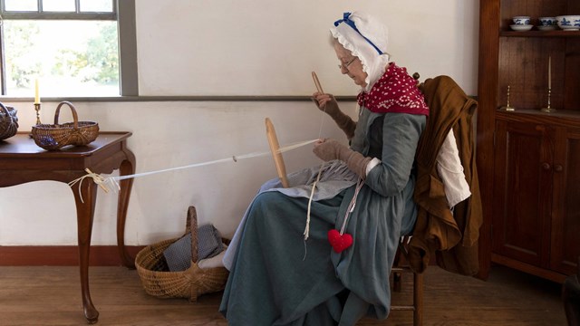 A park volunteer in colonial women's clothing weaving 