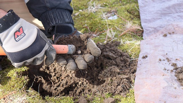 A small white musket ball is held in a had as a metal detector runs over it