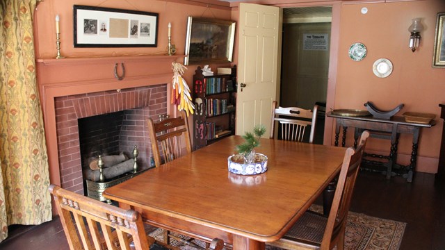 Historic dining room with table, chairs and a fireplace. Pink walls with sparse decoration.