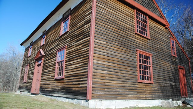 Two story wooden colonial house, unpainted with red trim viewed from the bottom looking up.