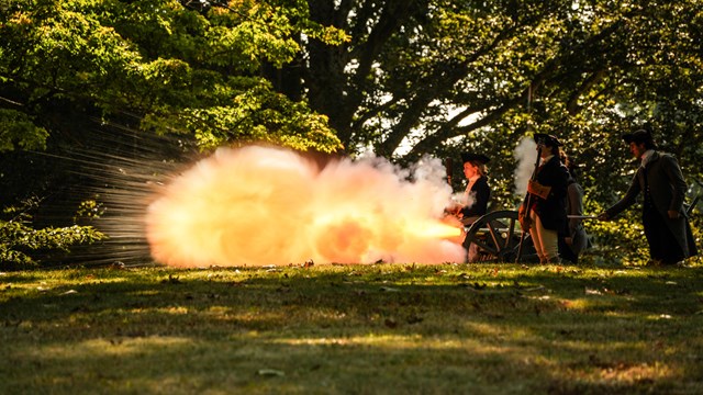 A large flash of fire comes from the front of a cannon.