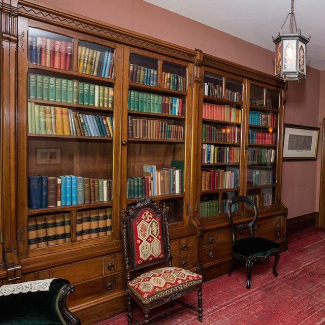 Library of The Wayside. 19th Century study with a red carpet, book shelves and a marble fireplace