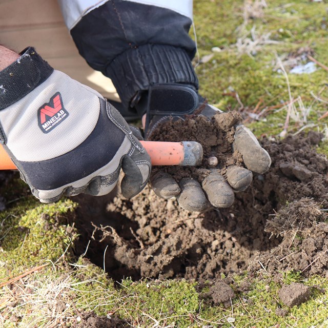 A small white musket ball is held in a had as a metal detector runs over it