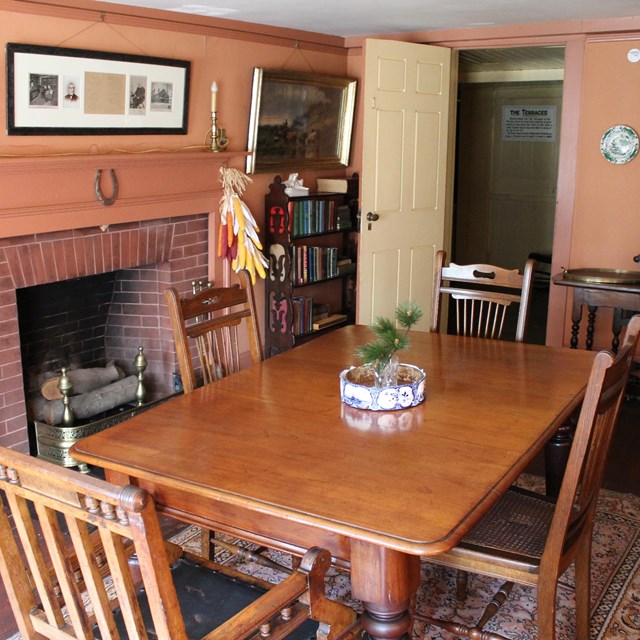 Historic dining room with table, chairs and a fireplace. Pink walls with sparse decoration.