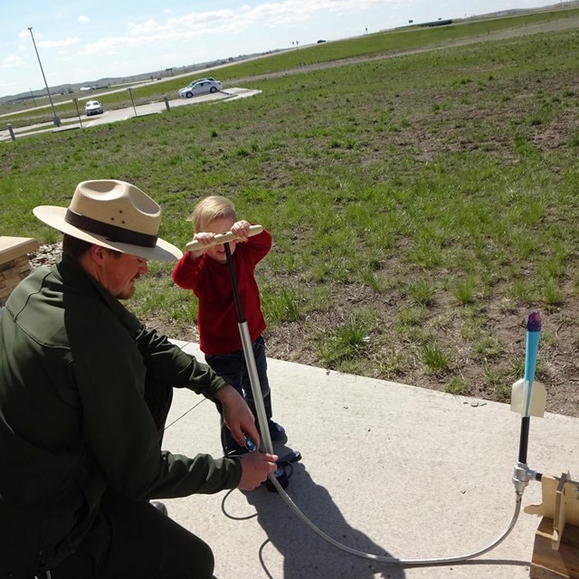A park ranger assists a young boy with launching a paper rocket