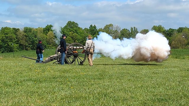 Reenactors dressed as Civil War soldiers fire a cannon.