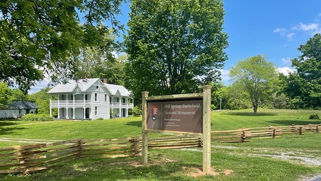 The NPS sign in front of a white house and green grass.