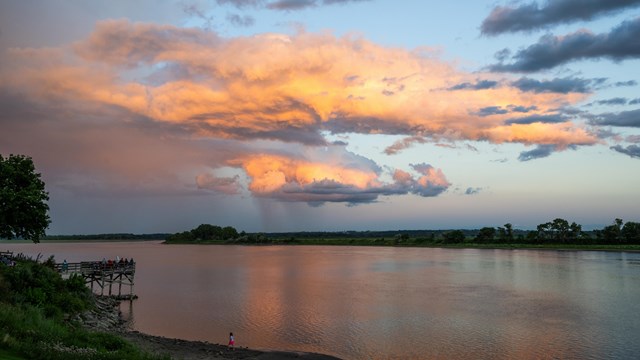 A view at sunset of a wide, flat river with colorful clouds in the sky
