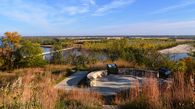 A concrete platform overlooking a river and bridge during fall