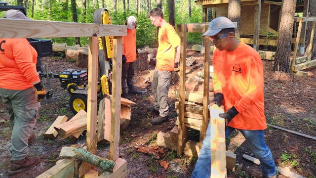 Four young students wearing orange shirts working outside