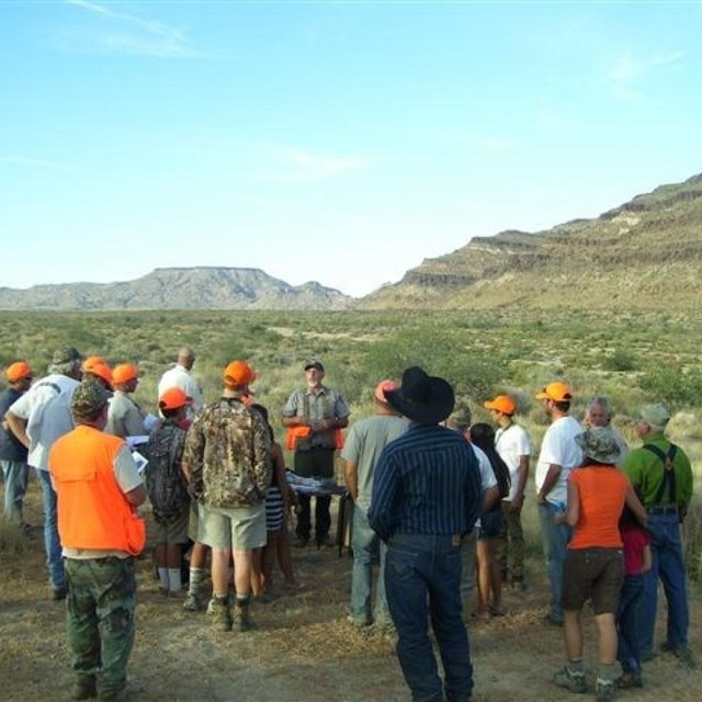 A group of parents and children in orange hats and vests gather for the Youth Quail Hunt with ranger