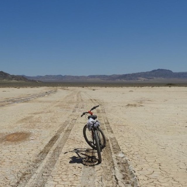 A bike in between tire tracks on Soda Dry Lake.  Mountains in the distance.