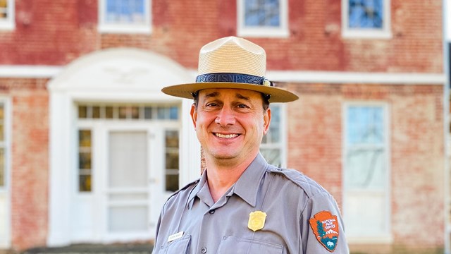 Superintendent Andrew Banasik stands in front of a red brick farmhouse.