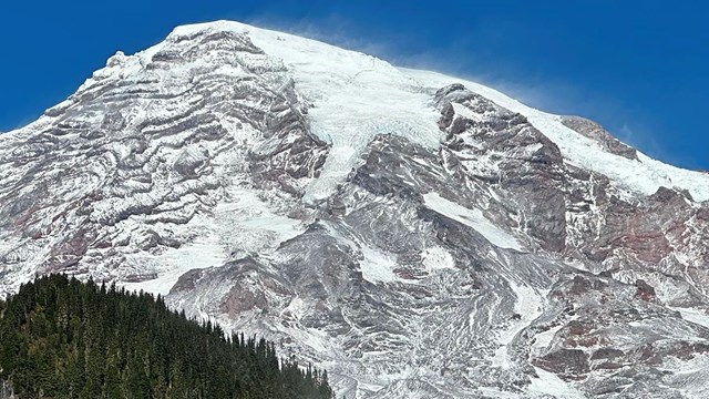 A snow-dusted mountain framed by forested ridges. 