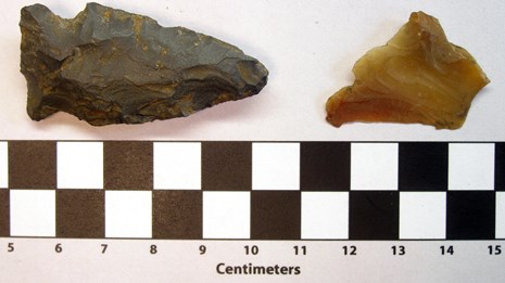 Two stone arrowheads on a white backgroun with a ruler below