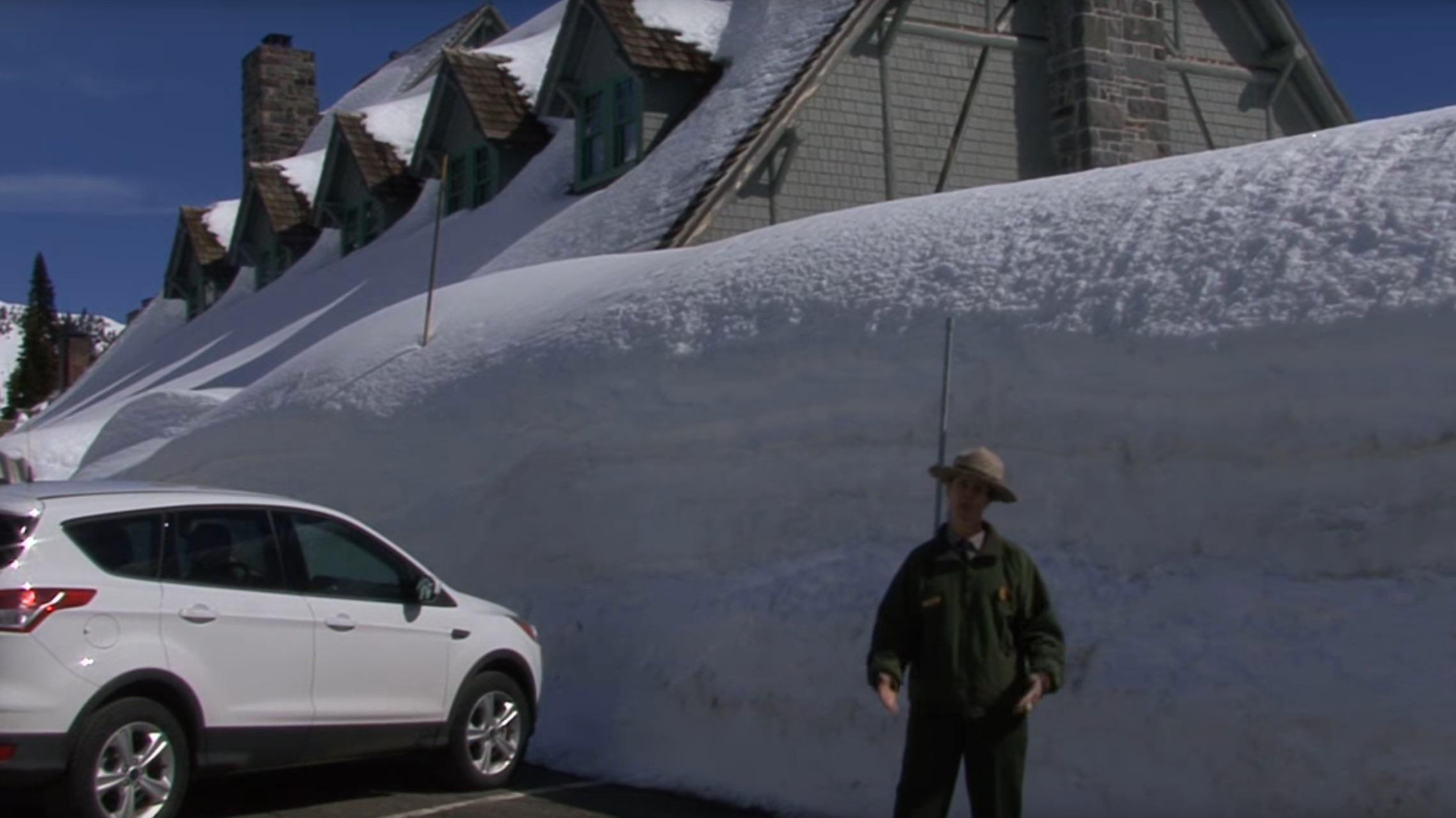 A ranger stands in front of a tall snowbank.