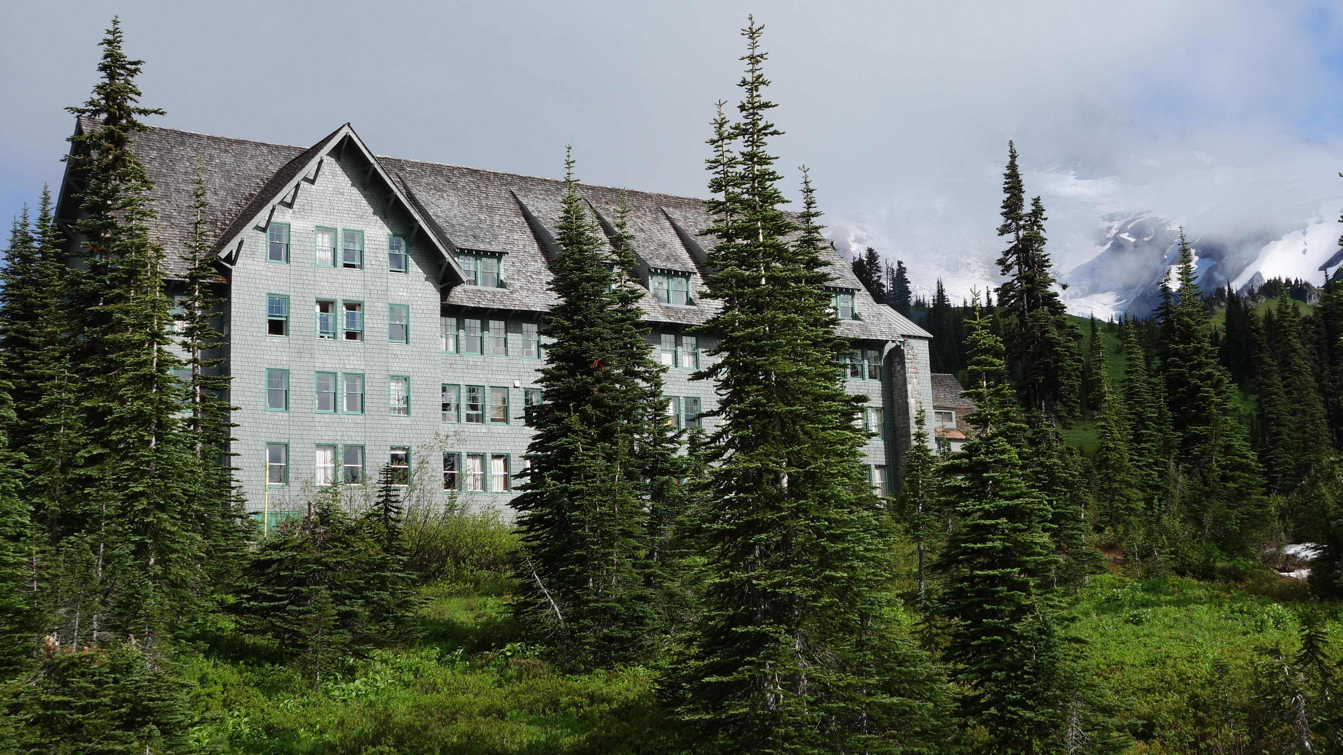 A multistory wood building framed by fir trees in front of a glaciated mountain.