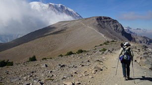 A hiker follows a trail along a ridge towards Mount Rainier. 