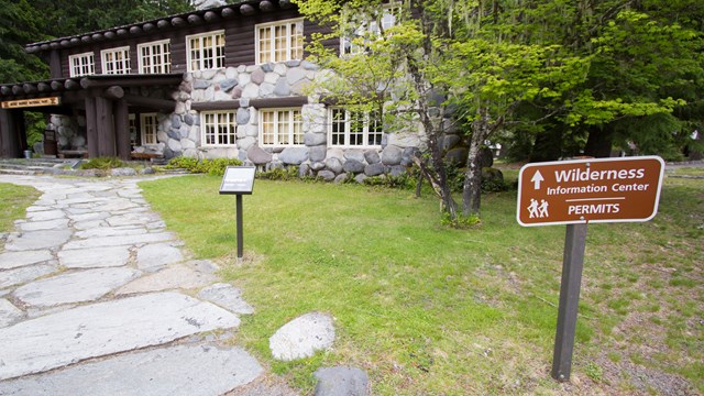 A sign next to a path leading to a rustic building reads "Wilderness Information Center - Permits".
