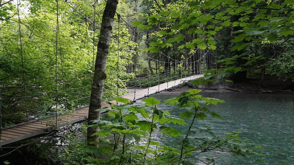 A narrow wood suspension bridge over a blue-green river. 