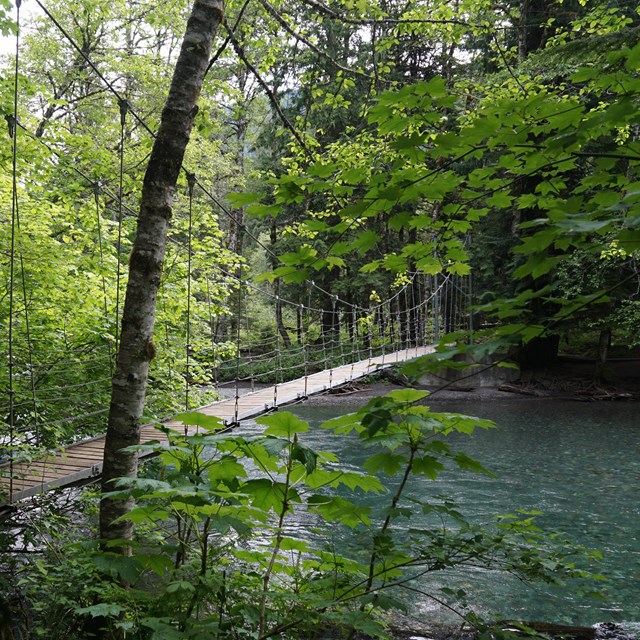 A narrow wood suspension bridge over a blue-green river. 