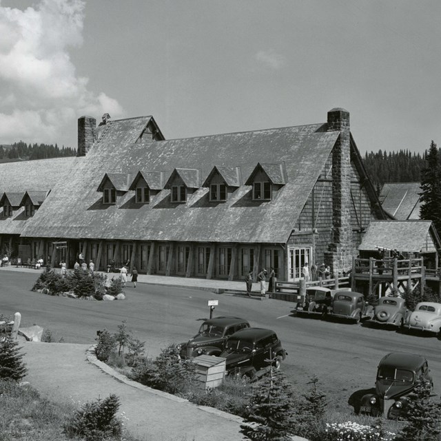 A large wood building with a shingle roof, gabled windows, stone fireplace and large parking lot.