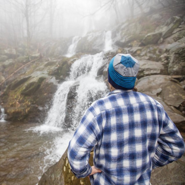 Visitor stands near a waterfall.