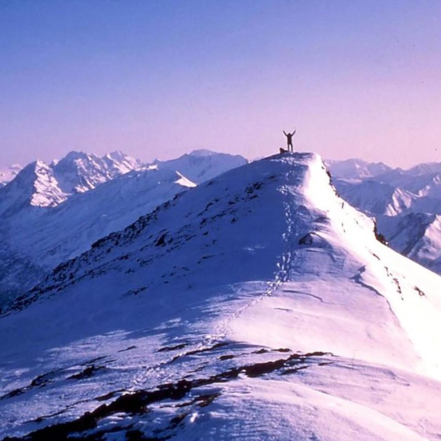 A man stands on top of a snowcapped mountain.