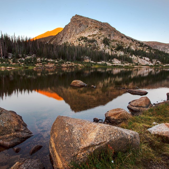 Sunrise casts an orange glow across Lawn Lake and the mountains behind it. 