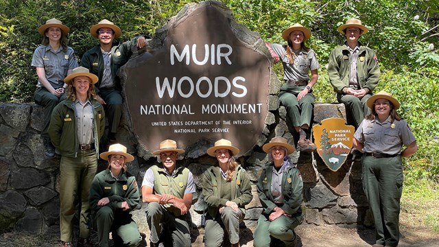 Two rangers stand on a trail in a redwood forest