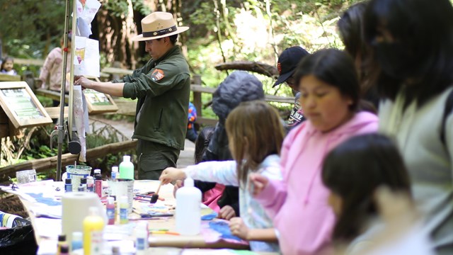 ranger and youth at activity table in the woods. 