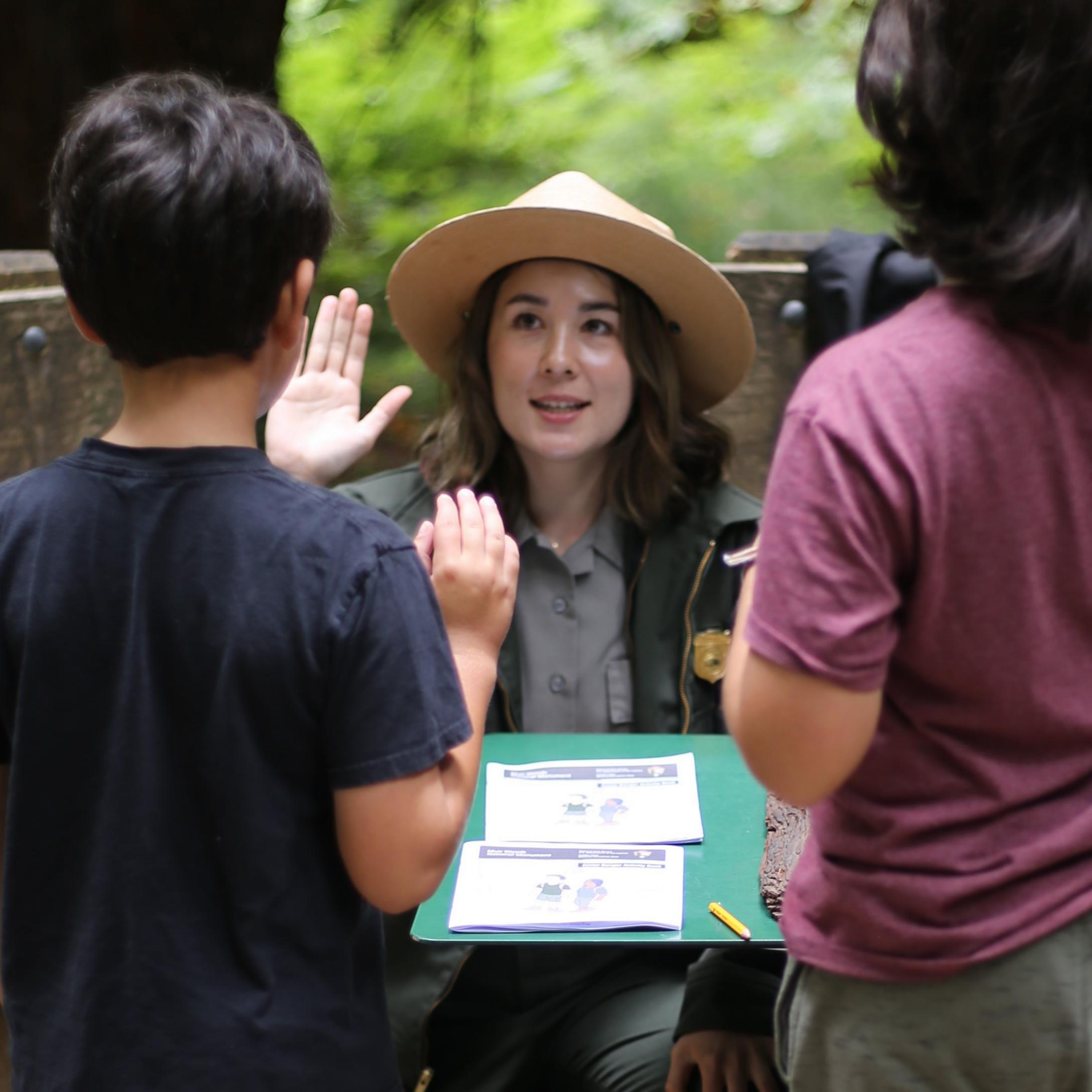 a uniformed ranger raises her right hand as she swears in two young junior rangers