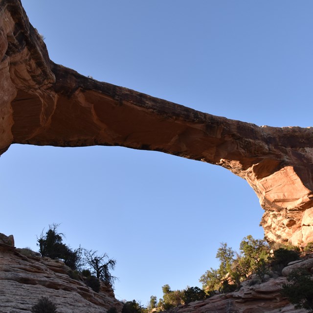 A thin beige and brown sandstone bridge spans across a blue sky