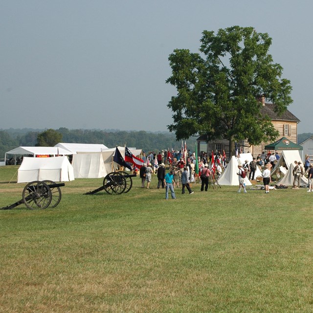 Crowd at a Civil War reeanctment camp with tents and cannons
