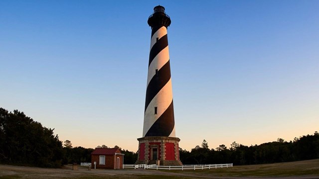 Black and white striped Cape Hatteras lighthouse with sunset behind