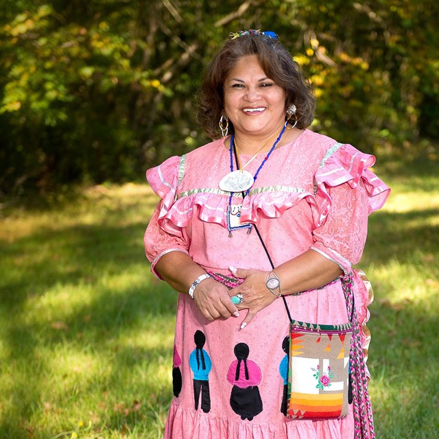 A tanned skin  woman in a pink dress with ruffles, beaded bag and Indian Jewelry