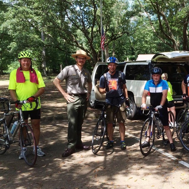 A group of 7 cyclists in bright colored shirts with a Park Ranger