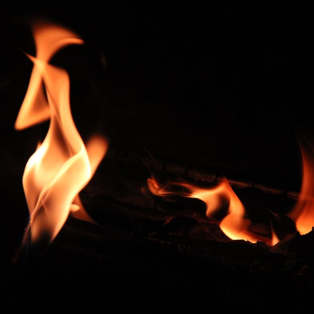 A natural flame shaped much like a human near smaller flames on a black background.