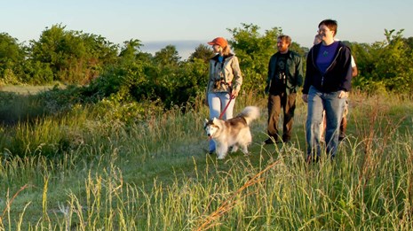 a family and their dog hike along a section of the trail in a prairie.