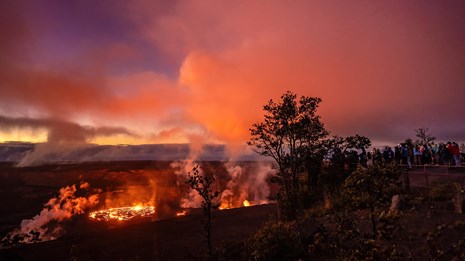 a glowing lava lake at sunset with a group of people observing from a cliff above