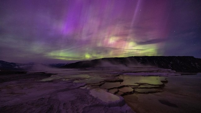 purples and greens of the northern lights above a hydrothermal feature at night